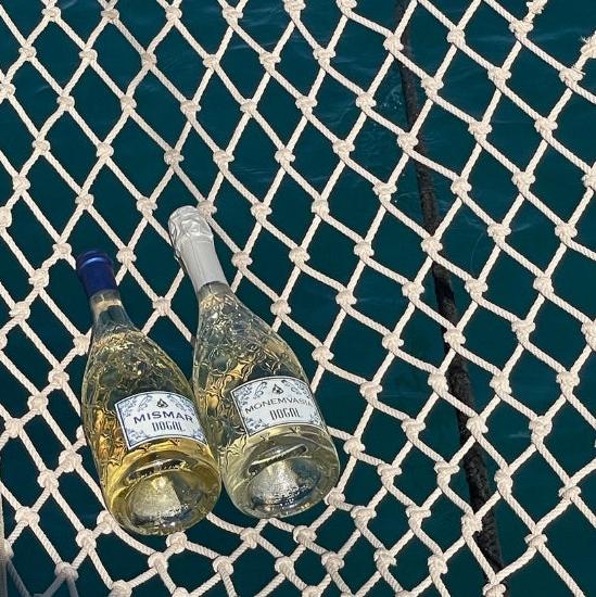 two bottles of Dogal Wine made with Malvasia lying on a net at the fron of a boat over the mediterranean sea